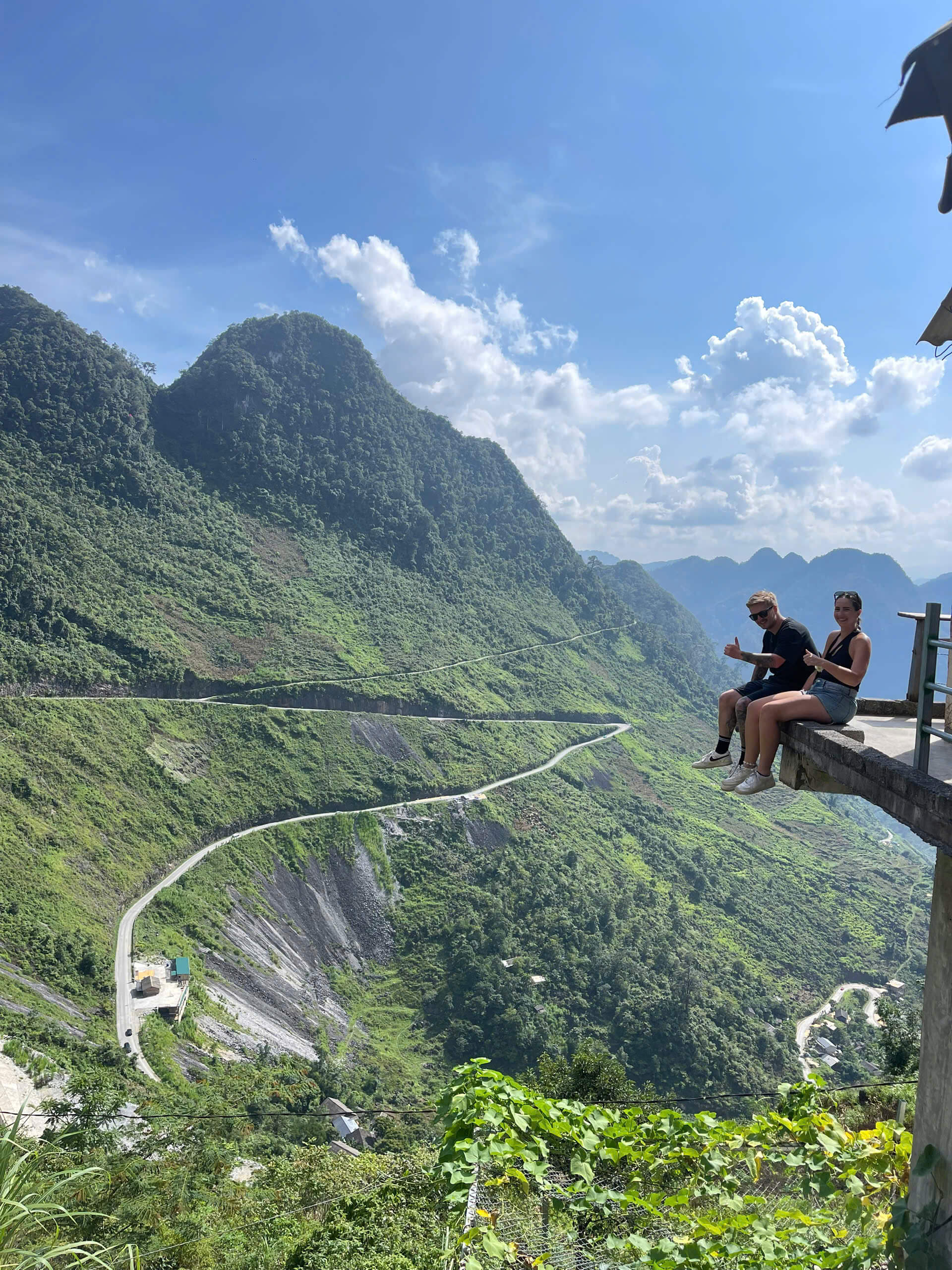 A spectacular landscape view of a white winding road snaking through a deep, lush green canyon at the Ma Pi Leng Pass in Ha Giang, Vietnam.