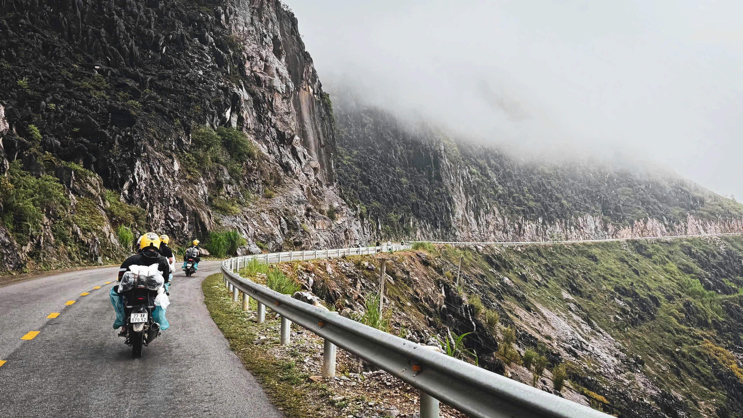 A group of Motorventures tourists and local Easy Riders safely navigating a rugged dirt road through a mountain valley on their Ha Giang motorbike adventure.
